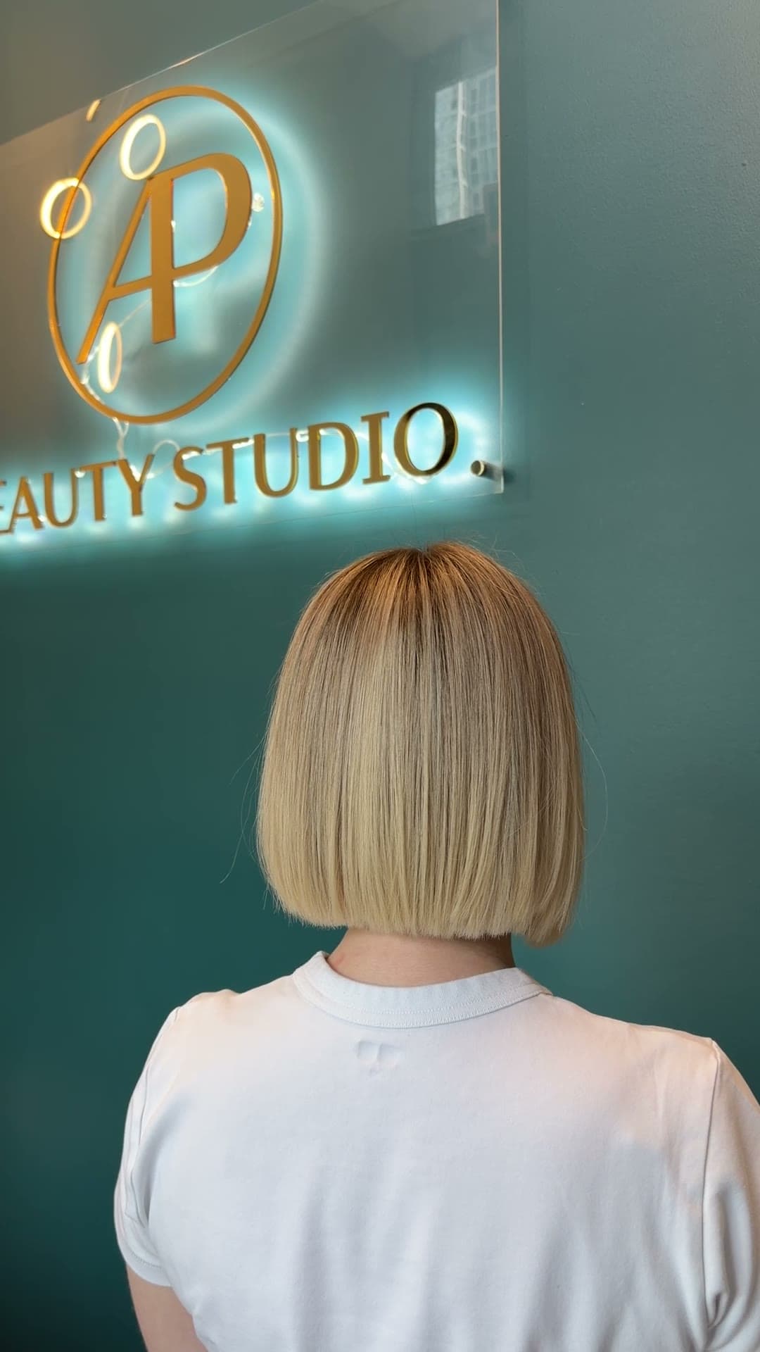 A sleek bob with a soft, blended root, in front of the AP Beauty Studio sign