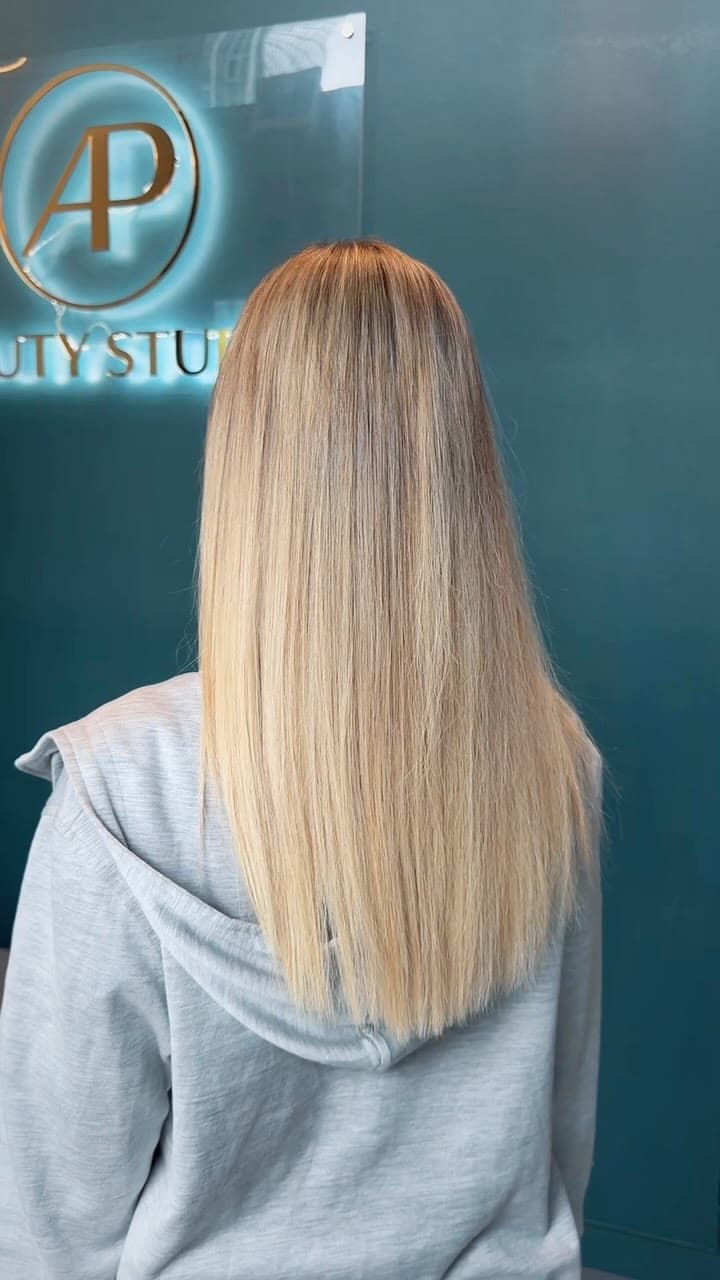 Long, straight blonde highlights seen from the back, in front of the AP Beauty Studio sign